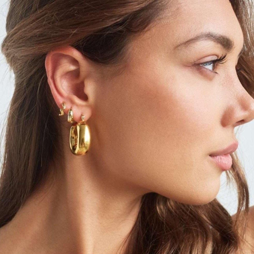 Model wearing large bold square shaped gold hoops 