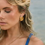 Model wearing 18k earrings shaped like a scroll or shell